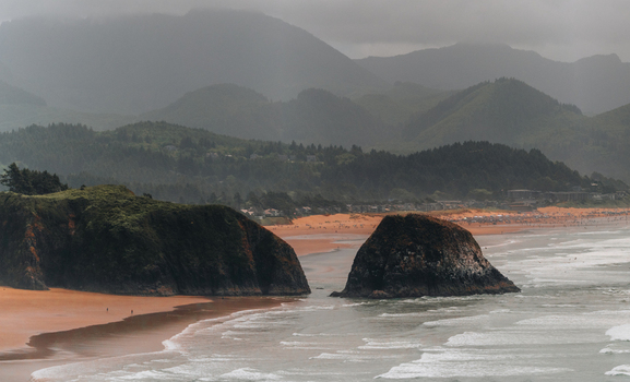 Aerial view of Haystack Rock on the sandy coastline of Cannon Beach with rolling waves lush green coastal mountains and a cloudy sky in Cannon Beach Oregon United States. Aerial view of Haystack Rock on the sandy coastline of Cannon Beach with rolling waves lush green coastal mountains and a cloudy sky in Cannon Beach Oregon United States.