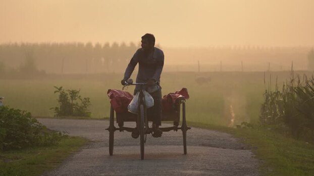 View of a man riding a cycle van on a misty road Bangladesh. View of a man riding a cycle van on a misty road Bangladesh.