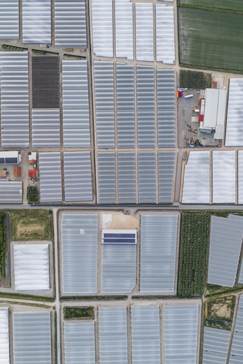 Aerial view of a vast greenhouse complex with geometric glass structures and solar panels on rooftops in Paestum Campania Italy.