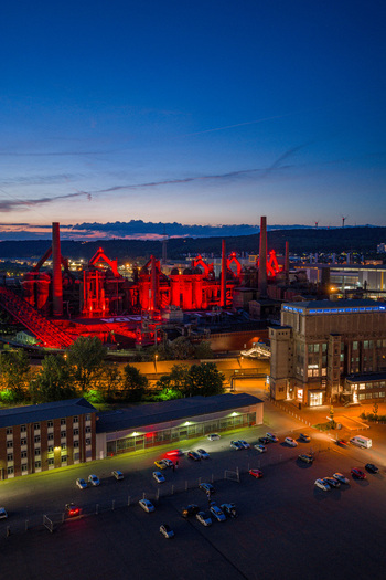 Volklingen Germany 09 May 2026 Aerial view of Volklingen Ironworks illuminated with red lights at dusk featuring blast furnaces industrial structures and a parking lot. Volklingen Germany 09 May 2026 Aerial view of Volklingen Ironworks illuminated with red lights at dusk featuring blast furnaces industrial structures and a parking lot.