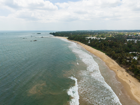Aerial view of a long sandy coastline with turquoise waves crashing on the shore and lush tropical palm trees in Matara Southern Province Sri Lanka. Aerial view of a long sandy coastline with turquoise waves crashing on the shore and lush tropical palm trees in Matara Southern Province Sri Lanka.