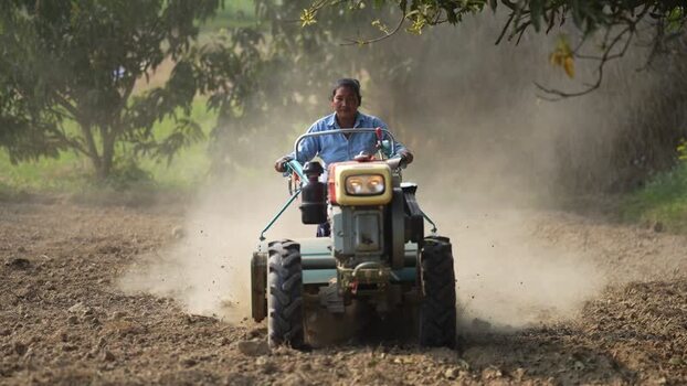 View of a woman operating a power tiller in a dusty field Nepal. View of a woman operating a power tiller in a dusty field Nepal.