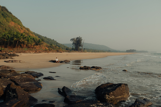 View of the tranquil beach with dark rocks contrasting against the sandy shore as gentle waves kiss the coastline Chiplun Maharashtra India. View of the tranquil beach with dark rocks contrasting against the sandy shore as gentle waves kiss the coastline Chiplun Maharashtra India.