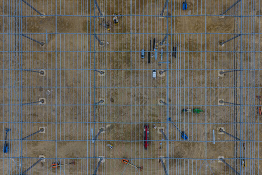 Aerial view of a steel frame structure under construction with metal beams and heavy machinery on a dirt site in the United Kingdom. Aerial view of a steel frame structure under construction with metal beams and heavy machinery on a dirt site in the United Kingdom.