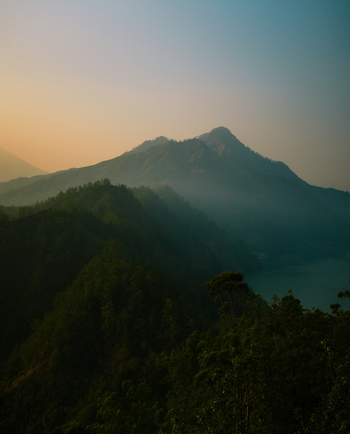 View of the misty volcanic landscape of Mount Batur with lush vegetation and a serene lake at sunrise in Kintamani Bali Indonesia.