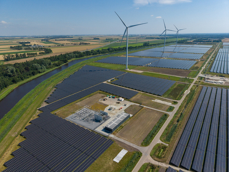 Aerial view of a large solar farm with rows of photovoltaic panels and wind turbines in a rural landscape in the Netherlands.
