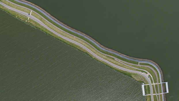 Aerial view of a winding road atop a dike separating two bodies of water with grassy banks and calm water surfaces in Uitdam North Holland Netherlands.