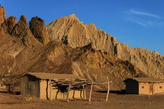 View of traditional mud houses nestled against the rugged sunlit rock formations of the Hingol landscape in Awaran Balochistan Pakistan.