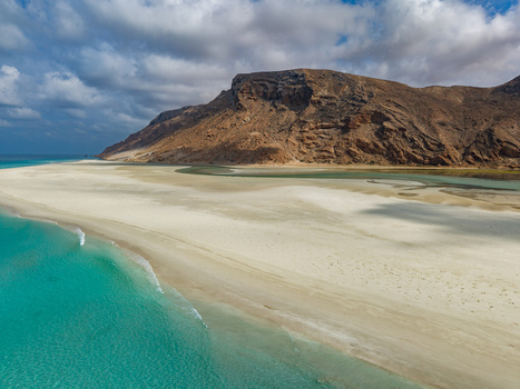 Aerial view of a sun kissed beach meeting the turquoise lagoon waters under a sky streaked with clouds Detwah lagoon Socotra Yemen.