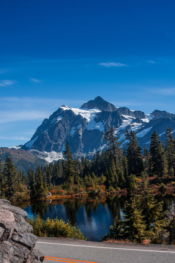 View of the snow capped Mount Baker reflecting in a calm lake surrounded by evergreen forests under a clear blue sky in Whatcom County Washington United States. View of the snow capped Mount Baker reflecting in a calm lake surrounded by evergreen forests under a clear blue sky in Whatcom County Washington United States.