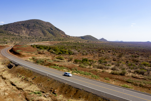 Aerial view of a car driving on a winding road through the arid landscape of Marsabit Marsabit County Kenya. Aerial view of a car driving on a winding road through the arid landscape of Marsabit Marsabit County Kenya.