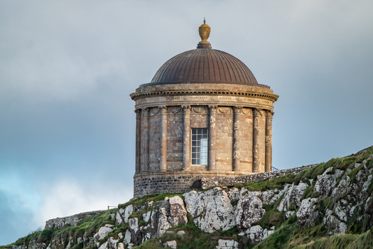 View of the historic Mussenden Temple perched on a cliff edge with stone columns and a dome overlooking the coast in Downhill Northern Ireland United Kingdom. View of the historic Mussenden Temple perched on a cliff edge with stone columns and a dome overlooking the coast in Downhill Northern Ireland United Kingdom.