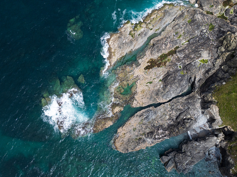 Aerial view of the rugged rocky coastline and turquoise sea with waves crashing against the cliffs at Godrevy Beach in Gwithian England United Kingdom. Aerial view of the rugged rocky coastline and turquoise sea with waves crashing against the cliffs at Godrevy Beach in Gwithian England United Kingdom.