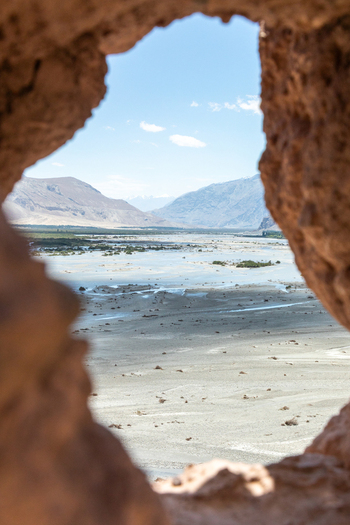 View of the landscape seen through a natural rock opening at Charasa Gonpa with a wide sandy riverbed and distant mountains in Charasa Ladakh India.
