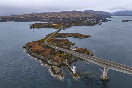 Aerial view of Skye Bridge spanning across the sea and Eilean Ban island with its white lighthouse under an overcast sky Isle of Skye Scotland United Kingdom.