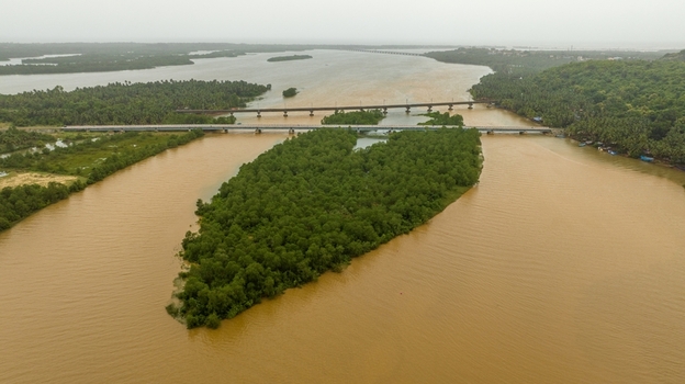 Aerial view of the lush green island in the Sharavathi River with bridges spanning the water surrounded by dense tropical vegetation under an overcast sky in Honnavar Karnataka India.