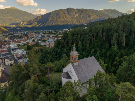 Aerial view of St. Laurentius Church nestled among trees overlooking the town of Imst with mountains in the background in Imst Tyrol Austria.
