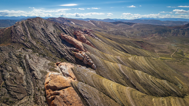 Aerial view of Gigantes Dormidos geological formations with dramatic layered sedimentary rock and arid mountain ridges under a blue sky in Tres Cruces Jujuy Province Argentina. Aerial view of Gigantes Dormidos geological formations with dramatic layered sedimentary rock and arid mountain ridges under a blue sky in Tres Cruces Jujuy Province Argentina.