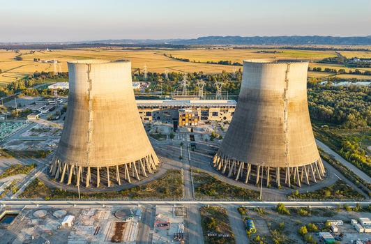 Aerial view of two massive cooling towers at an industrial power plant surrounded by electrical infrastructure farmland and transmission lines at golden hour. Italy. Aerial view of two massive cooling towers at an industrial power plant surrounded by electrical infrastructure farmland and transmission lines at golden hour. Italy.