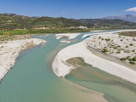Aerial view of Vjosa Wild River National Park with turquoise river waters white gravel riverbeds and green hills under a clear blue sky Permet Gjirokaster County Albania. Aerial view of Vjosa Wild River National Park with turquoise river waters white gravel riverbeds and green hills under a clear blue sky Permet Gjirokaster County Albania.