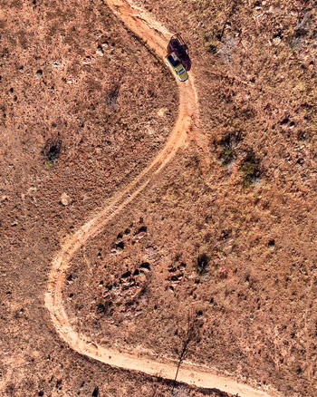 Aerial view of a utility 4x4 vehicle driving along a winding dirt track through the dry and remote wilderness in Vaalwater Limpopo South Africa.