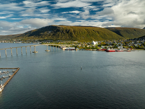 Aerial view of the Arctic Cathedral and Tromso Bridge spanning the water with mountains and coastal town buildings in Tromso Troms Norway.
