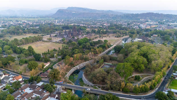 Aerial view of Prambanan Temple surrounded by lush greenery a winding river and a bridge in the foreground in Kecamatan Prambanan Daerah Istimewa Yogya Indonesia.