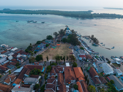 Aerial view of Karimunjawa Town Square featuring traditional terracotta roofed houses a busy harbor with small boats and turquoise waters in Karimunjawa Central Java Indonesia. Aerial view of Karimunjawa Town Square featuring traditional terracotta roofed houses a busy harbor with small boats and turquoise waters in Karimunjawa Central Java Indonesia.