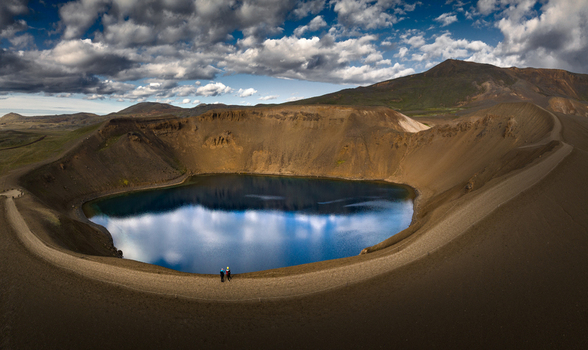 Aerial view of the Viti volcanic crater lake with deep blue water reflecting clouds and people standing on the rim in the Krafla area Iceland.