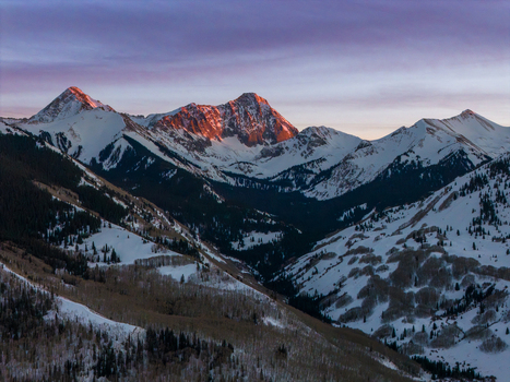 Aerial view of Capitol Peak in the Rocky Mountains during a winter sunset with snow covered slopes and evergreen forests in Aspen Colorado United States.