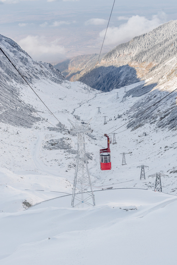 View of a red cable car traveling over a snow covered mountain valley with support towers along the Transfagarasan in Curtea de Arges Judetul Arges Romania. View of a red cable car traveling over a snow covered mountain valley with support towers along the Transfagarasan in Curtea de Arges Judetul Arges Romania.