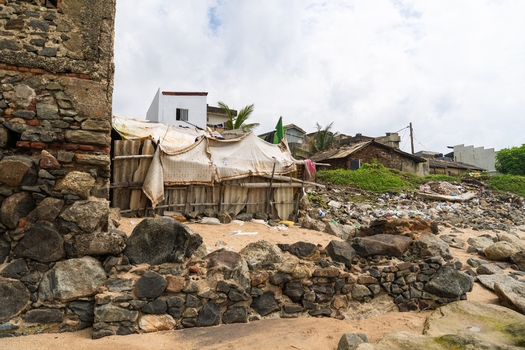 View of makeshift shelters and stone walls along a rocky coastal area under a cloudy sky in Galle Southern Province Sri Lanka.