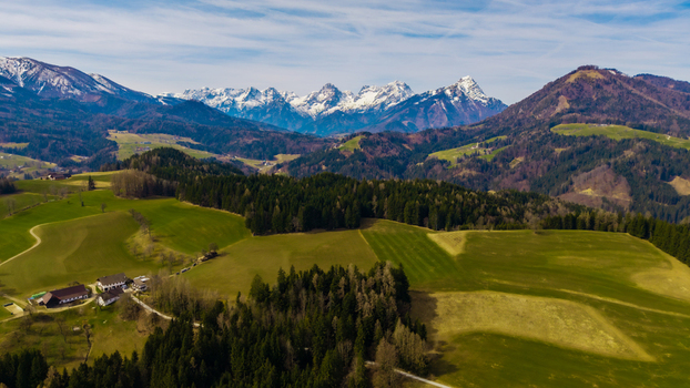Aerial view of rolling green hills meet snow capped peaks under a vast sky creating a contrast between the verdant valley and the majestic mountains Windischgarsten Upper Austria Austria. Aerial view of rolling green hills meet snow capped peaks under a vast sky creating a contrast between the verdant valley and the majestic mountains Windischgarsten Upper Austria Austria.