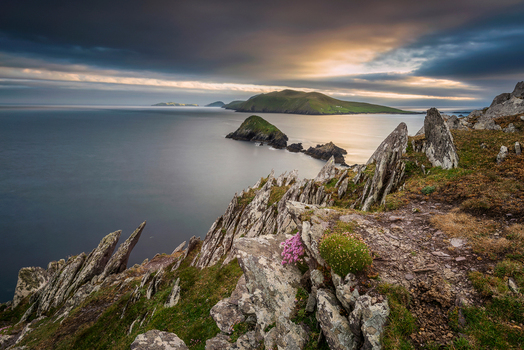 View of Dunmore Head with jagged rocks and coastal cliffs overlooking the Blasket Islands under a dramatic sunset sky in Ireland.