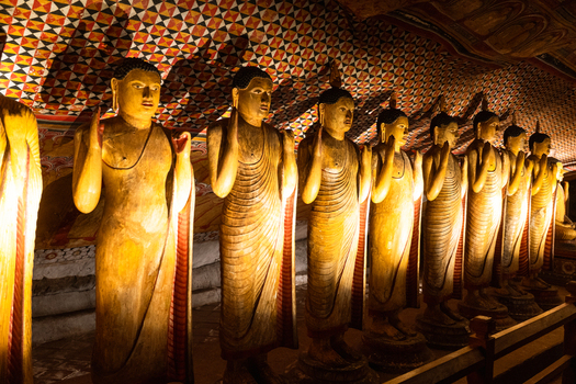 View of golden standing Buddha statues and intricate ceiling paintings inside the historic cave temple Dambulla Central Province Sri Lanka.