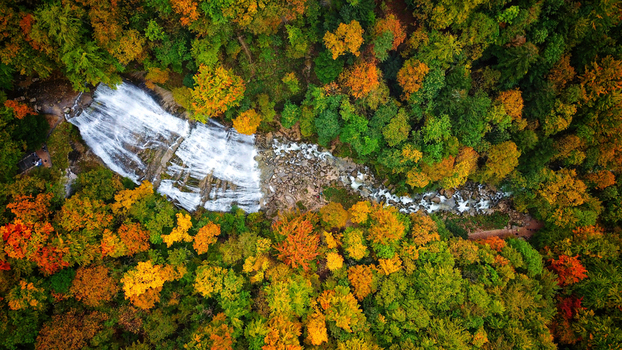 Aerial view of the cascading Herisson Waterfalls amidst the vibrant hues of autumn foliage a tapestry of green gold and russet Le Frasnois Bourgogne Franche Comt&eacute; France.