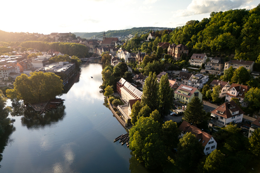 Aerial view of the Neckar river flowing through the historic old town with traditional houses and lush green trees under a warm sunset light in Tubingen Baden Wurttemberg Germany. Aerial view of the Neckar river flowing through the historic old town with traditional houses and lush green trees under a warm sunset light in Tubingen Baden Wurttemberg Germany.