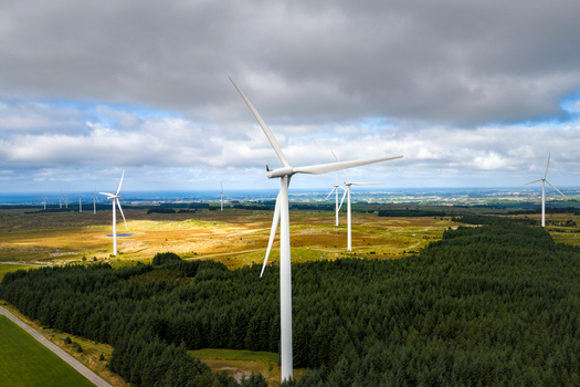 Aerial view of the Hog Jaeren wind farm with white wind turbines standing amidst green forests open fields and rolling hills under a cloudy sky in Ha Municipality Rogaland Norway. Aerial view of the Hog Jaeren wind farm with white wind turbines standing amidst green forests open fields and rolling hills under a cloudy sky in Ha Municipality Rogaland Norway.