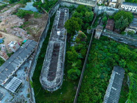 Aerial view of a long U shaped concrete structure surrounded by lush green trees and historic stone walls in Udaipur Rajasthan India.