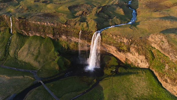 Aerial view of Seljalandsfoss waterfall cascading down mossy cliffs into a shadowy pool framed by vibrant green fields and a winding stream Seljalandsfoss Iceland. Aerial view of Seljalandsfoss waterfall cascading down mossy cliffs into a shadowy pool framed by vibrant green fields and a winding stream Seljalandsfoss Iceland.