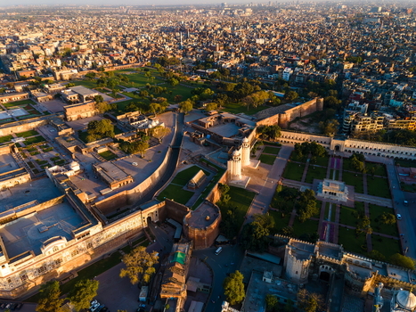 Aerial view of Lahore Fort featuring historic Mughal architecture lush green gardens and stone walls under golden hour light in Lahore Punjab Pakistan.