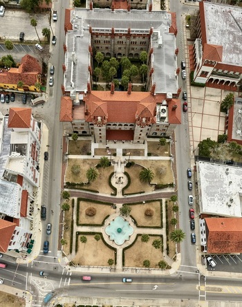 Aerial view of the historic Flagler College building featuring red tiled roofs a central courtyard with palm trees and a formal garden with a fountain in St. Augustine Florida United States.