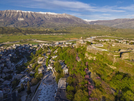 Aerial view of Gjirokaster Fortress overlooking the historic old town with stone architecture green hills and snow capped mountains in Gjirokaster Gjirokaster County Albania. Aerial view of Gjirokaster Fortress overlooking the historic old town with stone architecture green hills and snow capped mountains in Gjirokaster Gjirokaster County Albania.