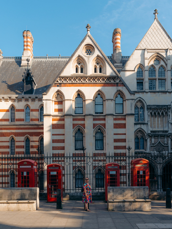 View of ornate Victorian architecture with striking red brick and white stone details framed by iconic red telephone booths and a lone figure London England United Kingdom. View of ornate Victorian architecture with striking red brick and white stone details framed by iconic red telephone booths and a lone figure London England United Kingdom.
