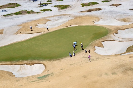 Aerial view of golfers and caddies on a putting green surrounded by extensive sand bunkers and dry grass in Juno Beach Florida United States. Aerial view of golfers and caddies on a putting green surrounded by extensive sand bunkers and dry grass in Juno Beach Florida United States.