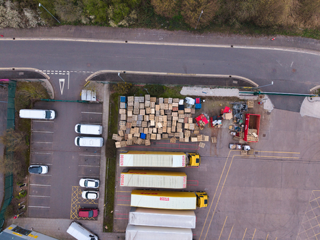 Aerial view of trucks and stacked boxes create a geometric pattern of yellow brown and grey contrasting with the surrounding tarmac Northampton United Kingdom. Aerial view of trucks and stacked boxes create a geometric pattern of yellow brown and grey contrasting with the surrounding tarmac Northampton United Kingdom.