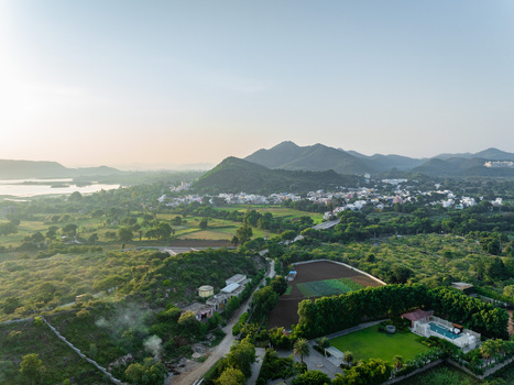 Aerial view of the lush landscape surrounding the city with rolling hills green fields scattered residential buildings and a swimming pool in the foreground in Udaipur Rajasthan India.