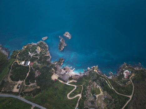 Aerial view of the Tonnara di Scopello with its historic buildings and rocky stacks in turquoise water along the lush green coastline Scopello Sicily Italy.