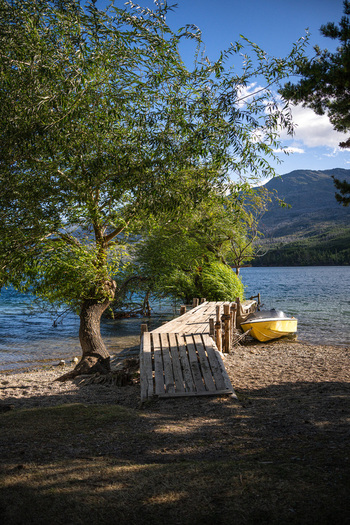 View of Lago Puelo National Park with a wooden pier and a yellow boat moored on the shore surrounded by willow trees and mountains in Cushamen Chubut Argentina.