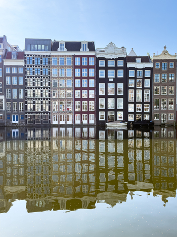 View of the iconic colorful canal houses with their tall narrow facades reflecting in the calm water of the canal under a clear blue sky in Amsterdam North Holland Netherlands. View of the iconic colorful canal houses with their tall narrow facades reflecting in the calm water of the canal under a clear blue sky in Amsterdam North Holland Netherlands.